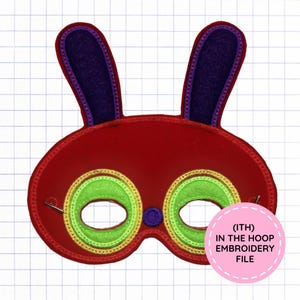 May include: A red felt mask featuring two tall purple ears with red borders, lime green eye patches with gold stitching, and a small purple nose. A pink circular label in the bottom right corner displays the text (ITH) IN THE HOOP EMBROIDERY FILE.