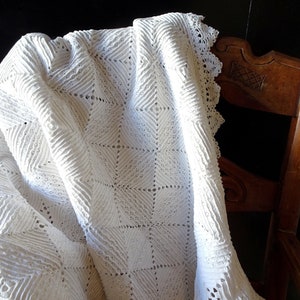 May include: A white crocheted throw blanket with a delicate lace trim draped over a wooden chair.
