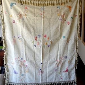 May include: A white tablecloth with embroidered birds, butterflies and flowers in various colours. The tablecloth has a fringed border.