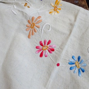 May include: White linen tablecloth with embroidered flowers in shades of pink, orange, yellow, and blue.