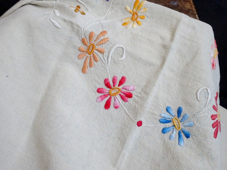 May include: White linen tablecloth with embroidered flowers in shades of pink, orange, yellow, and blue.
