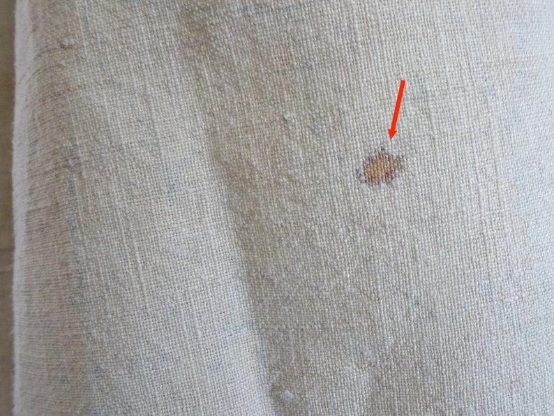 May include: Close-up of a beige fabric with a small brown stain. The stain is in the centre of the image and is surrounded by a light beige fabric.