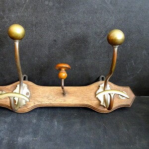 Peut inclure: Un porte-manteau en bois avec trois crochets en laiton. Les crochets ont des boutons ronds en laiton sur le dessus. Le porte-manteau est de couleur brun clair et a une finition légèrement vieillie.