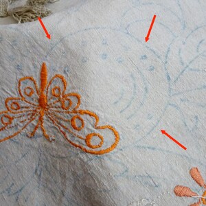 May include: A white linen tablecloth with embroidered details. The embroidery includes a butterfly, flowers, and leaves. The embroidery is done in orange, blue, and pink thread.