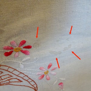 May include: White linen tablecloth with embroidered pink and red flowers. The tablecloth has several small, light brown stains.