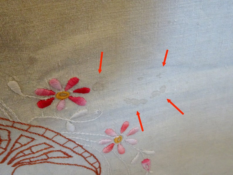 May include: White linen tablecloth with embroidered pink and red flowers. The tablecloth has several small, light brown stains.