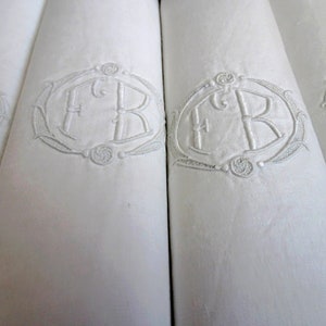 Puede incluir: Cuatro servilletas de lino blanco con iniciales bordadas "F.R." en un marco ovalado decorativo.