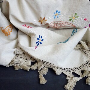 May include: A white linen tablecloth with embroidered flowers and butterflies. The tablecloth has a crocheted edge with tassels.