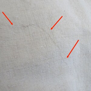May include: Close-up of a white fabric surface with three small, thin, dark lines. The lines are visible due to the texture of the fabric.