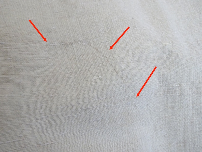 May include: Close-up of a white fabric surface with three small, thin, dark lines. The lines are visible due to the texture of the fabric.