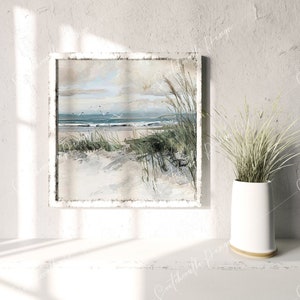 May include: A white framed painting depicting a beach scene with blue water, white sand, and green grass. The painting is on a white wall with a white vase containing green plants in front of it.