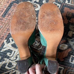 May include: A pair of green suede platform heels with brown soles. The heels are ankle strap sandals with a chunky heel.