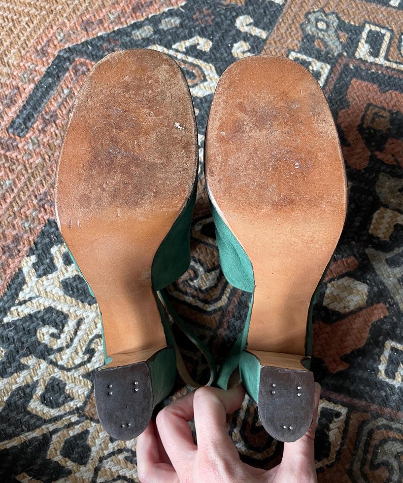 May include: A pair of green suede platform heels with brown soles. The heels are ankle strap sandals with a chunky heel.