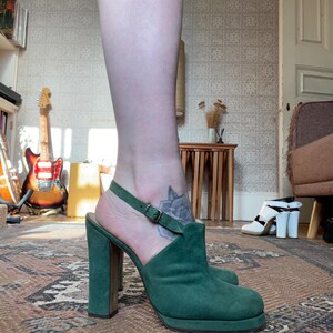 May include: Green suede platform heels with a buckle ankle strap. The heels are approximately 4 inches tall.