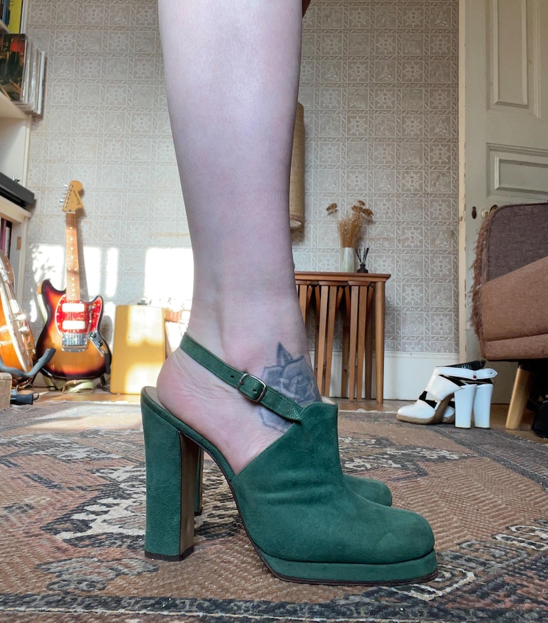 May include: Green suede platform heels with a buckle ankle strap. The heels are approximately 4 inches tall.