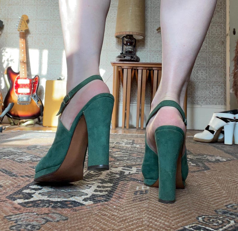 May include: A pair of green suede platform heels with a chunky heel. The heels have a peep toe and an ankle strap.