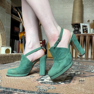 May include: A pair of green suede platform heels with ankle straps. The heels are about 4 inches tall and have a chunky platform.