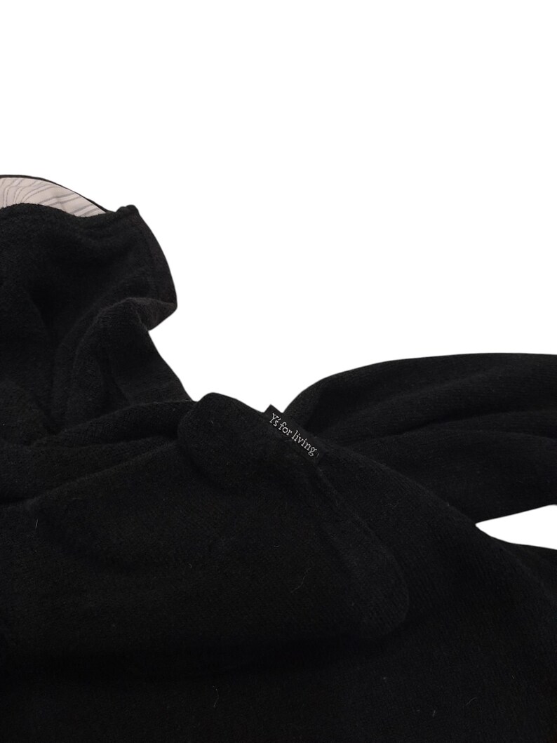 Puede incluir: Una prenda negra con capucha y superficie suave y texturizada. Una peque&ntilde;a etiqueta de tela negra est&aacute; unida al lateral, con el texto blanco Y's for living. El interior de la capucha est&aacute; forrado con una tela clara con finas rayas verticales.