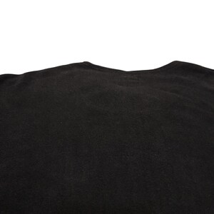 Puede incluir: Una camiseta negra lisa con un cuello redondo sencillo y mangas cortas. El tejido tiene una textura mate consistente en toda la prenda, mostrando la parte superior de la misma desde el cuello hasta la zona del pecho en un estilo sencillo.