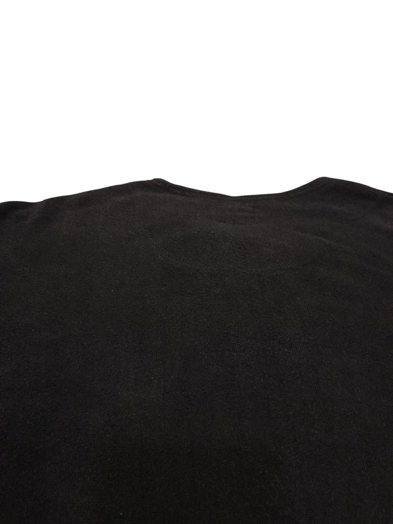 Puede incluir: Una camiseta negra lisa con un cuello redondo sencillo y mangas cortas. El tejido tiene una textura mate consistente en toda la prenda, mostrando la parte superior de la misma desde el cuello hasta la zona del pecho en un estilo sencillo.