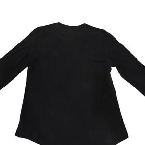 Puede incluir: Una camiseta de manga larga en color negro s&oacute;lido con un escote redondeado y un dobladillo ligeramente curvado. La prenda est&aacute; confeccionada con un tejido liso y opaco de tono oscuro uniforme, presentando un dise&ntilde;o sencillo y funcional.