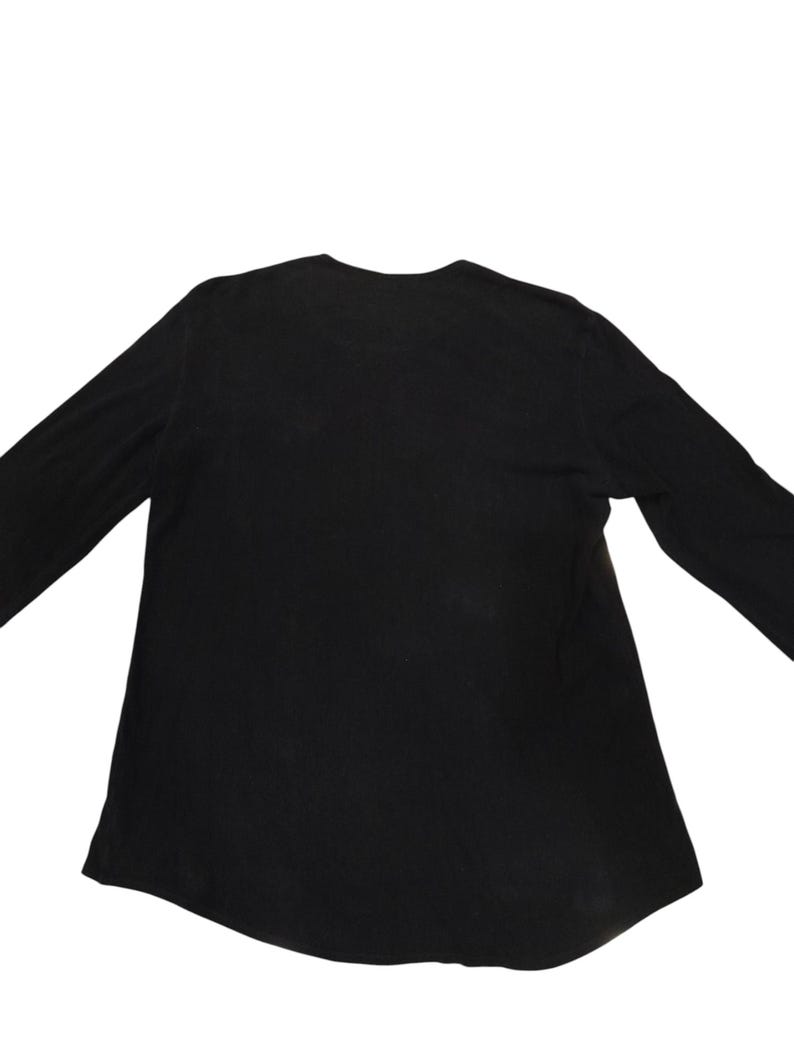Puede incluir: Una camiseta de manga larga en color negro s&oacute;lido con un escote redondeado y un dobladillo ligeramente curvado. La prenda est&aacute; confeccionada con un tejido liso y opaco de tono oscuro uniforme, presentando un dise&ntilde;o sencillo y funcional.