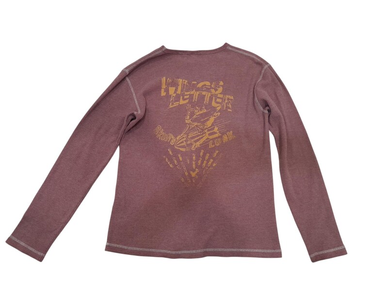 May include: A long-sleeve mauve shirt with visible white stitching along the seams. The back features a gold-toned graphic print with the text "WINGS LETTER" above an illustration of a winged object and the word "LUCK" below the graphic.