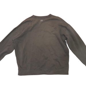 May include: A dark gray sweatshirt with long sleeves. The crew neck sweatshirt has a small white logo near the neckline. The garment is made of a soft material and is laid flat.