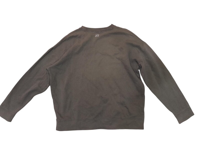 May include: A dark gray sweatshirt with long sleeves. The crew neck sweatshirt has a small white logo near the neckline. The garment is made of a soft material and is laid flat.