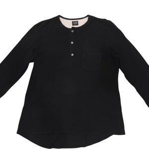 Puede incluir: Una camiseta henley negra de manga larga con una tapeta de tres botones, un bolsillo en el pecho y un dobladillo redondeado. El forro interior del cuello es blanco con finas rayas verticales negras e incluye una etiqueta que dice Y's FOR LIVING.