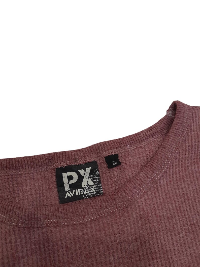 May include: A mauve thermal knit long-sleeve shirt with a ribbed crew neckline. A black rectangular label is sewn inside the collar featuring the white text PX AVIREX. A smaller black tag next to it indicates the size as XL.