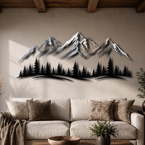 Könnte beinhalten: Ein Wandkunstobjekt aus Metall, das ein silberfarbenes Gebirge mit gezackten, schneebedeckten Gipfeln über einer dichten, schwarzen Silhouette eines Nadelwaldes zeigt. Das Design ist länglich und horizontal angeordnet und wirkt geschichtet.