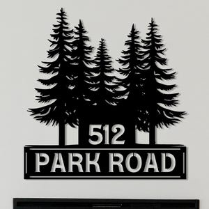 May include: Black metal address sign featuring a silhouette of pine trees above the numbers "512" and the words "PARK ROAD". The sign is mounted on a white wall above a fireplace and a gray sofa.