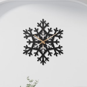 May include: A black snowflake-shaped wall clock with gold hands hanging on a white wall above a white couch with pillows and a coffee table.