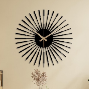 May include: A black and gold sunburst clock with a minimalist design hangs on a beige wall above a dining table with four chairs. The table is made of wood and has a concrete top. The chairs are made of wood and have a woven seat.