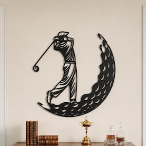 Puede incluir: Una pieza de arte mural de metal negro que presenta la silueta de un golfista en movimiento de swing, integrada en un dise&ntilde;o circular grande y texturizado de una pelota de golf. La obra est&aacute; montada en una pared clara sobre un mueble de madera.