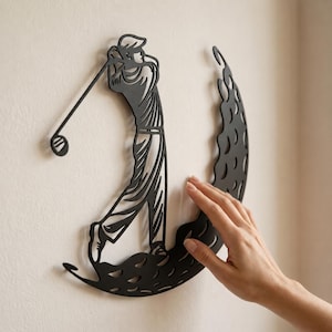 Puede incluir: Una pieza de arte mural de metal negro que presenta la silueta de un golfista en movimiento de swing. El dise&ntilde;o incluye una base curva y estilizada con un patr&oacute;n texturizado que recuerda la superficie de una pelota de golf.