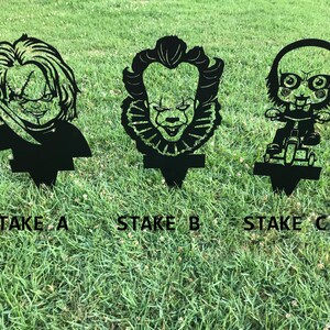K&ouml;nnte beinhalten: Drei schwarze Metall-Gartenpf&auml;hle mit Horrorfilmfiguren. Die Pf&auml;hle sind mit "Stake A", "Stake B" und "Stake C" beschriftet.