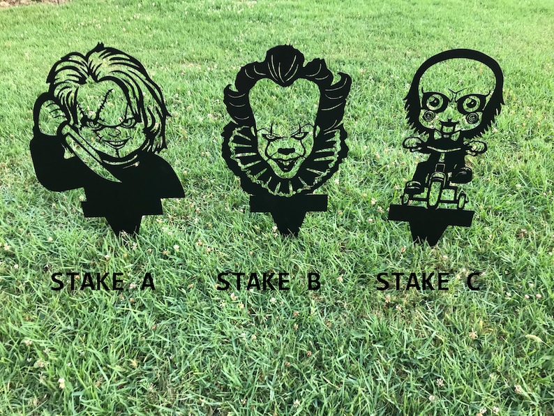 K&ouml;nnte beinhalten: Drei schwarze Metall-Gartenpf&auml;hle mit Horrorfilmfiguren. Die Pf&auml;hle sind mit "Stake A", "Stake B" und "Stake C" beschriftet.
