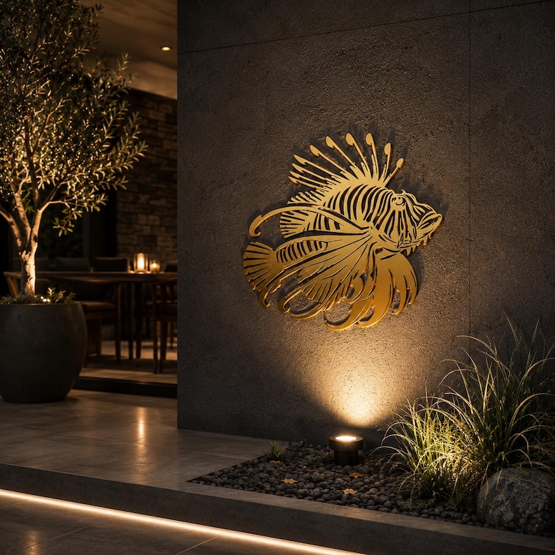 Puede incluir: Una pieza de arte mural de metal dorado con forma de pez le&oacute;n con detalles intrincados y fluidos en las aletas. El dise&ntilde;o recortado presenta espinas afiladas y un cuerpo texturizado, montado sobre una pared de piedra gris oscuro iluminada.
