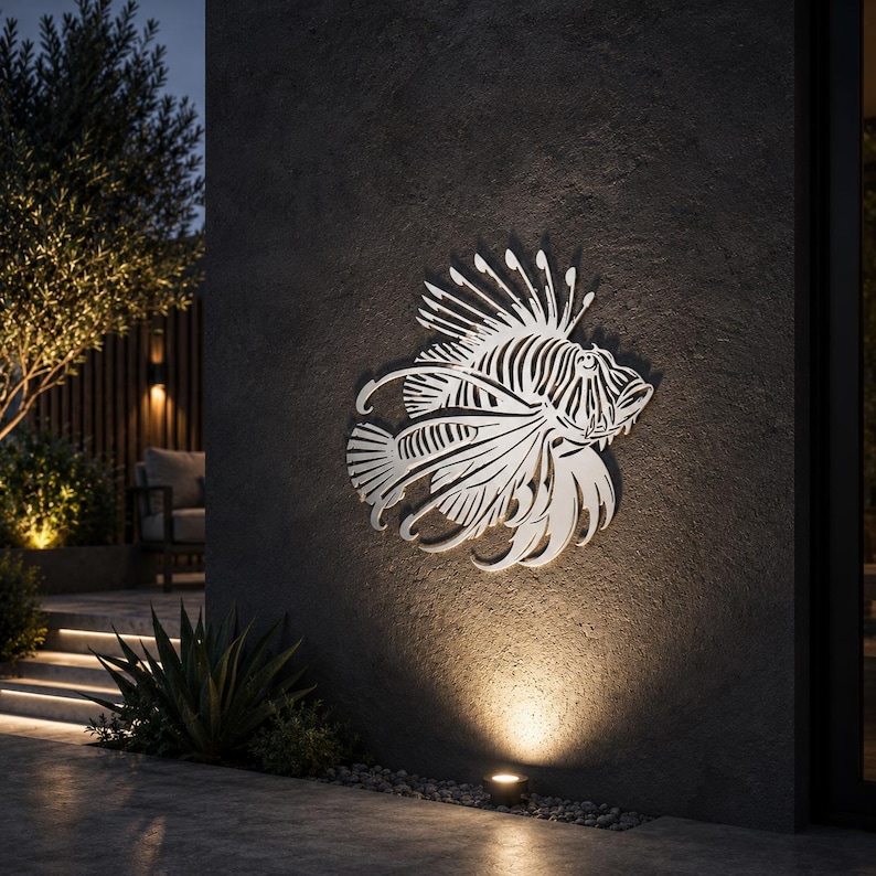 Puede incluir: Una pieza de arte mural de metal en tono plateado con forma de pez le&oacute;n, que presenta intrincados detalles recortados que definen sus aletas, espinas y estructura corporal. La escultura est&aacute; montada plana sobre una pared exterior oscura.