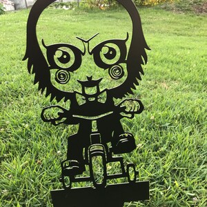 K&ouml;nnte beinhalten: Schwarze Metallsilhouette eines Comic-Charakters, der ein Dreirad f&auml;hrt. Der Charakter hat gro&szlig;e Augen und ein verschmitztes Grinsen. Die Silhouette ist so konzipiert, dass sie in einem Garten oder Hof platziert werden kann.
