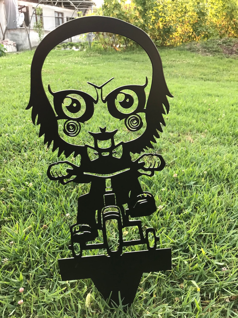 K&ouml;nnte beinhalten: Schwarze Metallsilhouette eines Comic-Charakters, der ein Dreirad f&auml;hrt. Der Charakter hat gro&szlig;e Augen und ein verschmitztes Grinsen. Die Silhouette ist so konzipiert, dass sie in einem Garten oder Hof platziert werden kann.