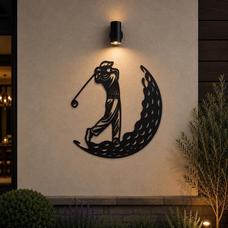 Puede incluir: Una pieza de arte mural de metal negro que presenta la silueta de un golfista en pleno movimiento de swing. El golfista est&aacute; posicionado dentro de una forma de media luna texturizada con hendiduras circulares, imitando una pelota de golf.
