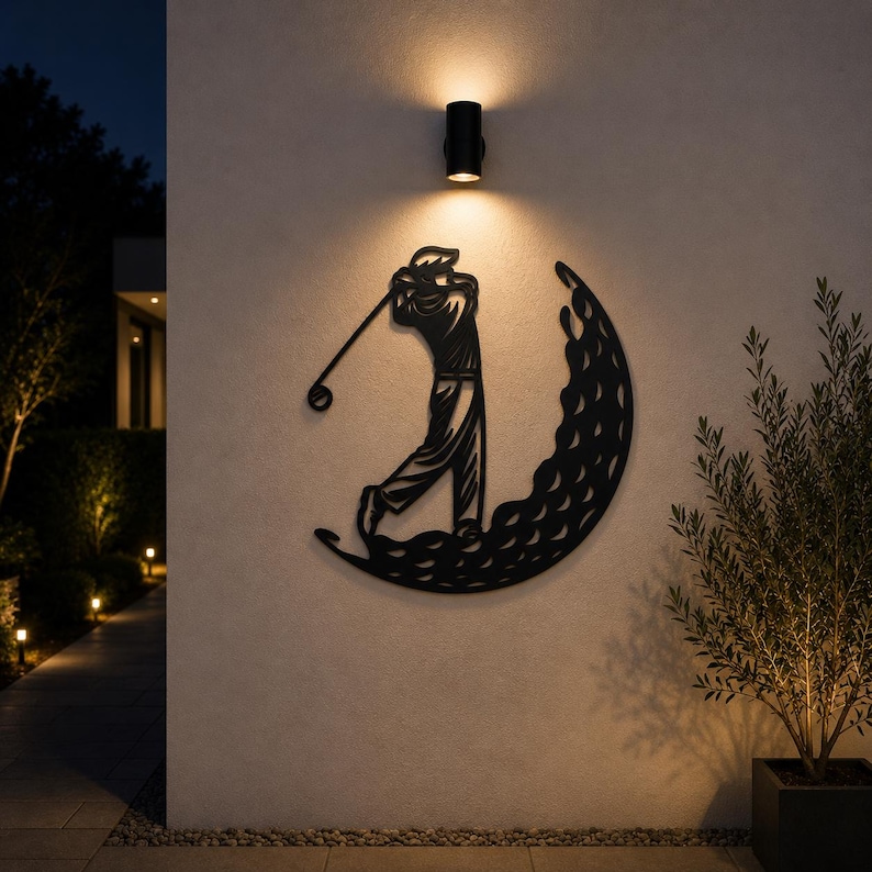 Puede incluir: Una pieza de arte mural de metal negro que presenta la silueta de un golfista en pleno swing, integrada en una forma de media luna con un patr&oacute;n texturizado que recuerda a los hoyuelos de una pelota de golf, montada en una pared exterior clara.