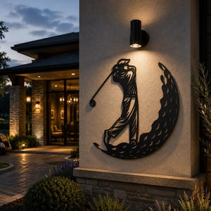 Puede incluir: Una pieza de arte mural de metal negro con la silueta de un golfista en pleno swing, integrada en un dise&ntilde;o circular que recuerda a una pelota de golf con textura. La pieza est&aacute; montada en una pared exterior clara bajo una luz cil&iacute;ndrica.