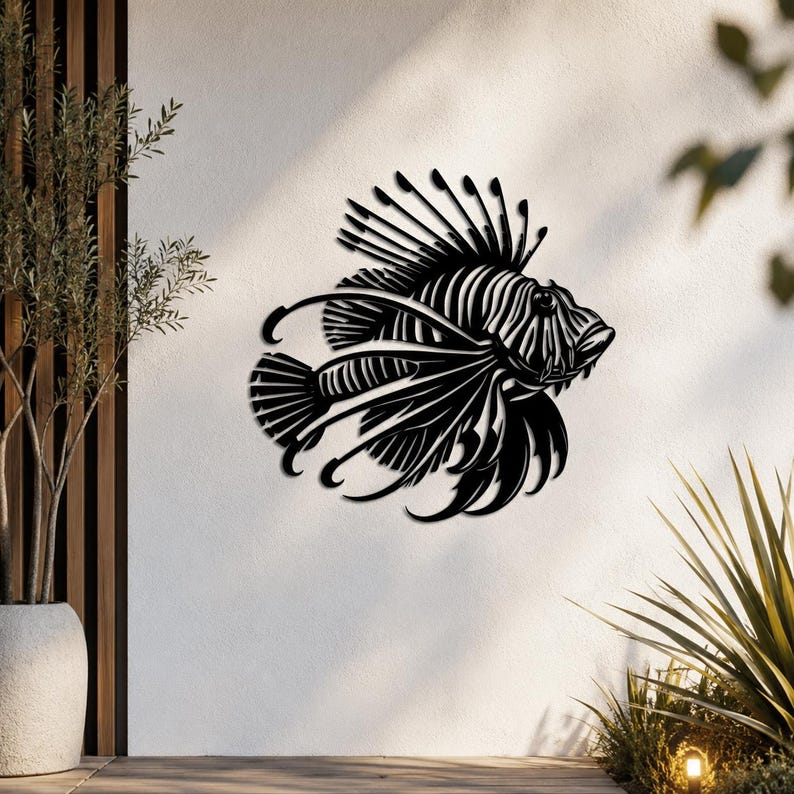 Puede incluir: Una pieza de arte mural de metal negro con forma de pez le&oacute;n, que presenta recortes intrincados que definen las aletas espinosas, el cuerpo rayado y la cabeza detallada del pez. La silueta est&aacute; montada sobre una superficie vertical clara.