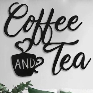 Puede incluir: Arte de pared de metal negro con las palabras "Coffee and Tea" en una fuente cursiva. La palabra "Coffee" est&aacute; encima de "Tea". Una taza con un dise&ntilde;o de vapor en forma de coraz&oacute;n aparece con la palabra "AND" en el medio.