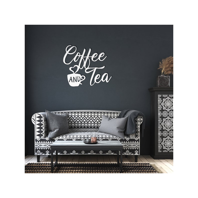 Puede incluir: Arte de pared blanco con las palabras "Coffee and Tea" en fuente cursiva, con un coraz&oacute;n y un s&iacute;mbolo de taza de caf&eacute;. El arte est&aacute; montado en una pared azul oscuro sobre un sof&aacute; con un patr&oacute;n geom&eacute;trico en blanco y negro.