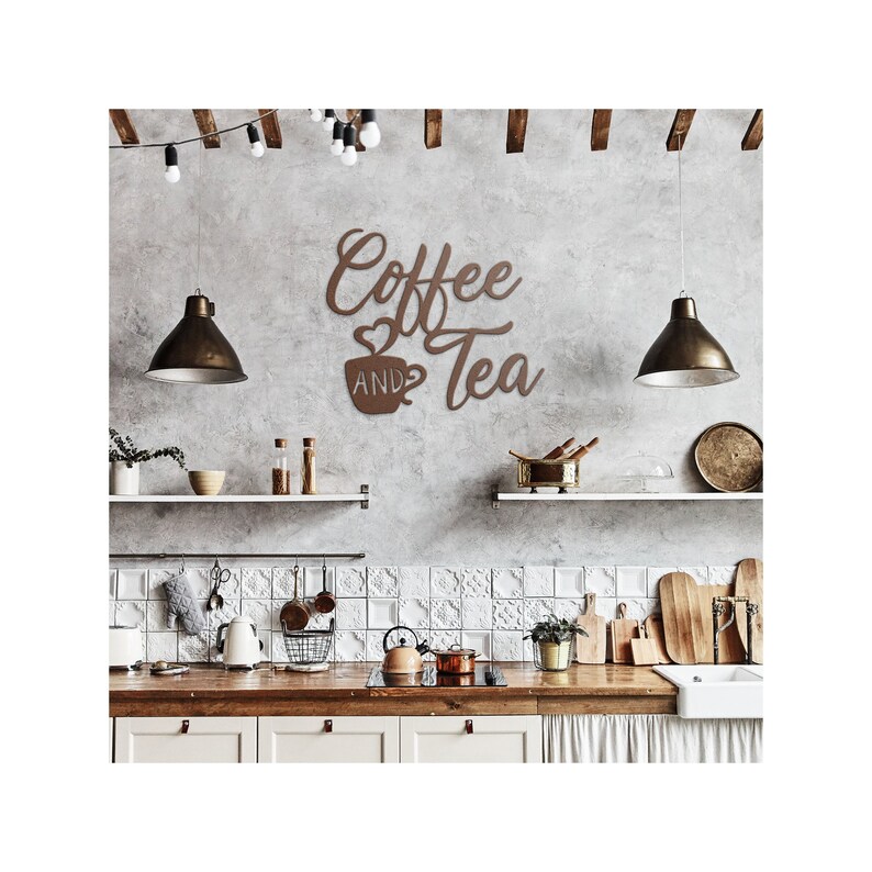 Puede incluir: Un letrero de pared de metal marr&oacute;n que dice "Coffee and Tea" en escritura cursiva, con un gr&aacute;fico de taza de caf&eacute;. El letrero est&aacute; montado en una pared gris texturizada en un entorno de cocina, con luces colgantes y estantes.